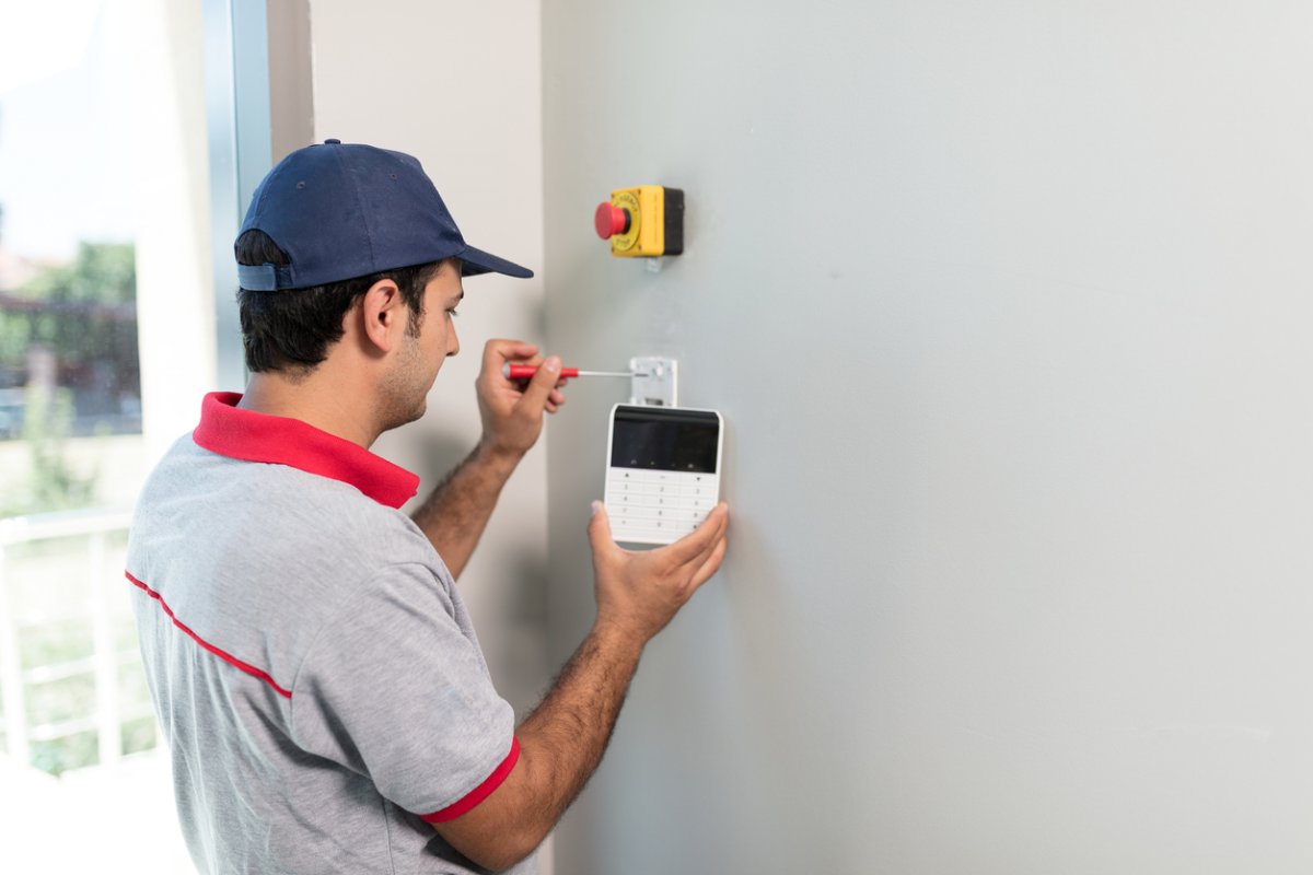 A worker installs a control panel for a security system.