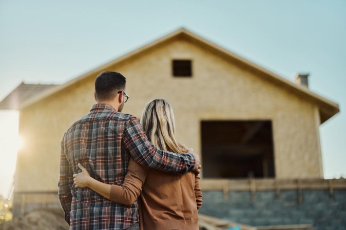 A couple is seen embracing in front of a beige house.