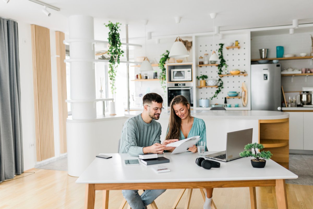 A man and a woman look over documents while seated at a kitchen table. 