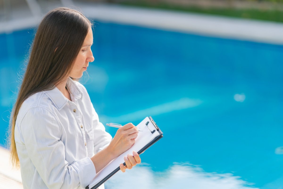 A person checks items on a list while assessing a pool.