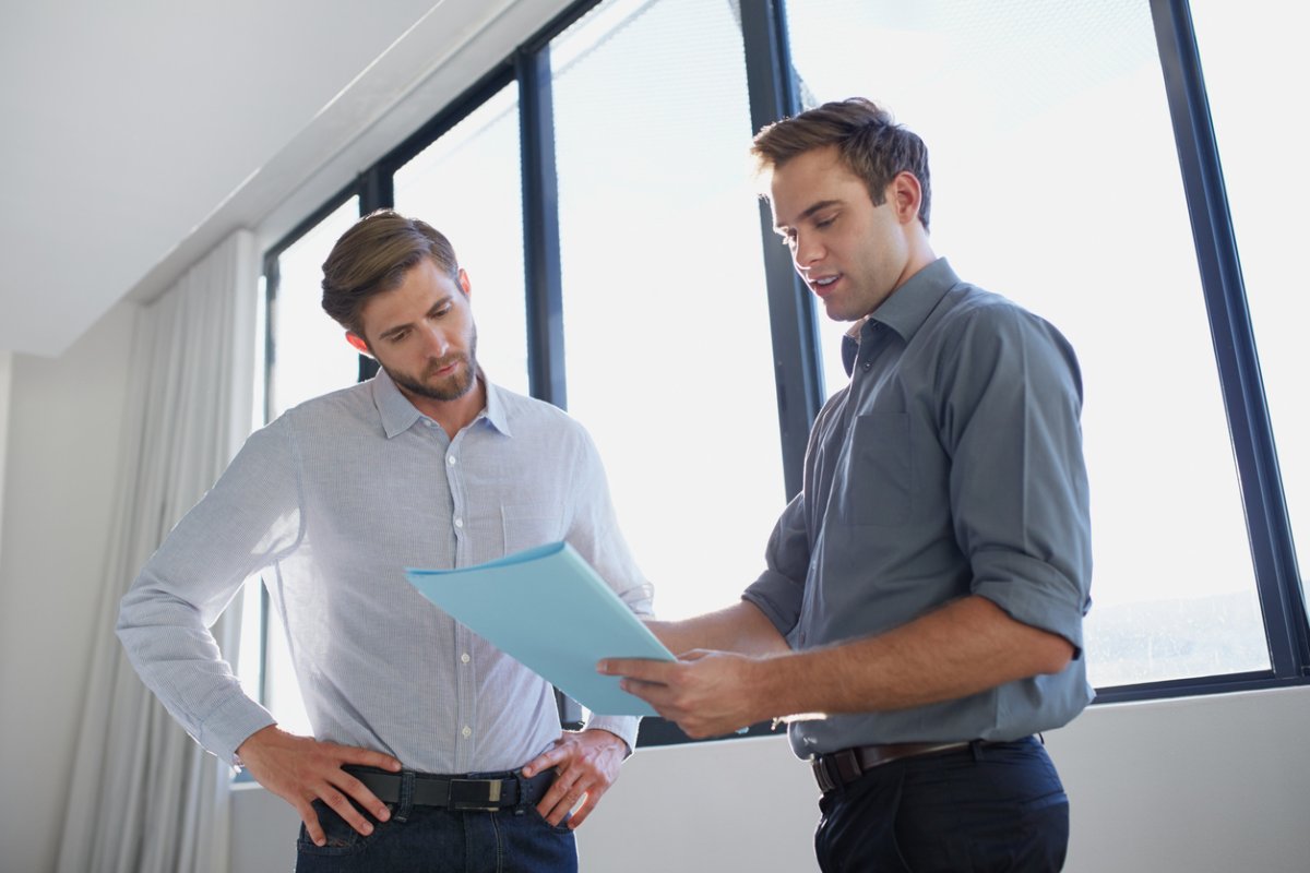 Two men converse over a blue document.