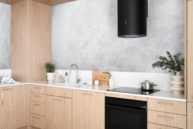 A light wood kitchen with a black cylindrical oven range hood.