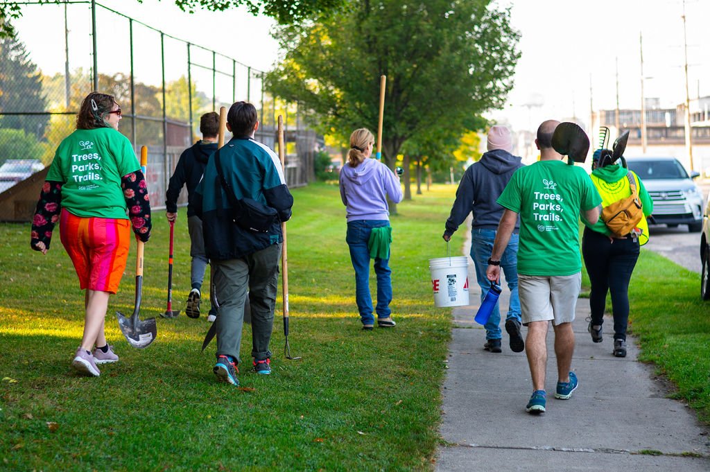 A group of people walk with shovels and buckets down a sidewalk for an Arbor Day activity in Grand Rapids.