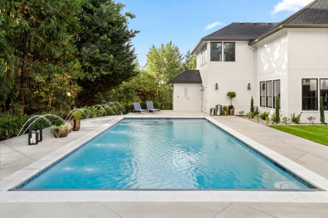 A view of a pool by a beautiful house on a bright and sunny day.