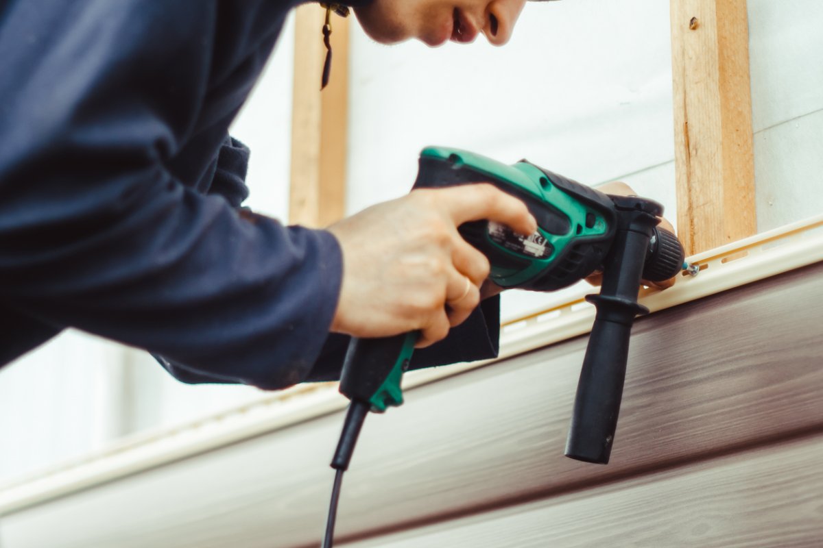 A worker installs panels beige siding on the facade of the house.