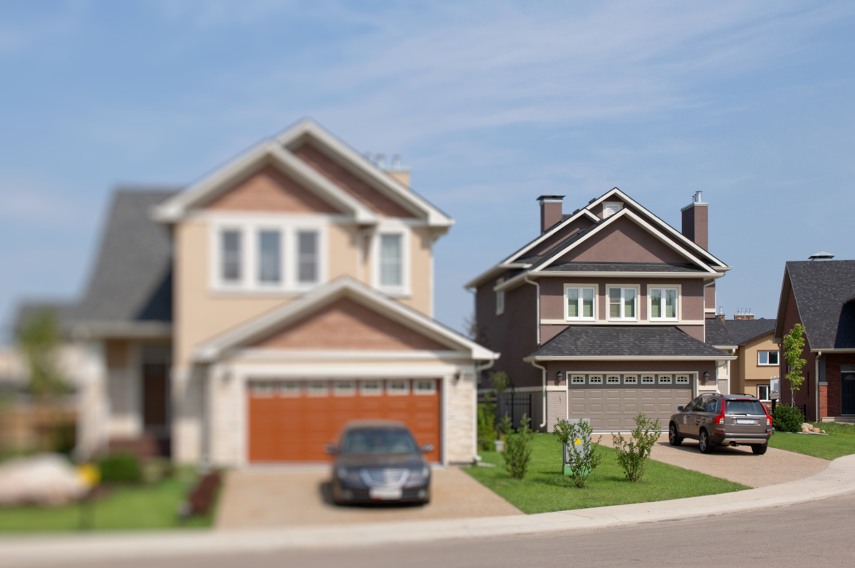 Two new-construction two-story houses in a typical suburban neighborhood. One is blurred out and the other is not.