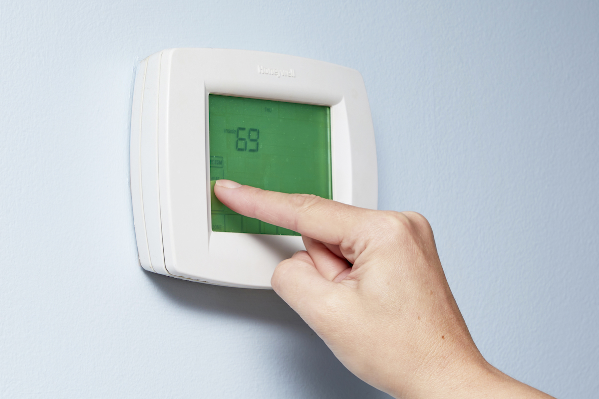 Woman adjusts the temperature on a digital thermostat.