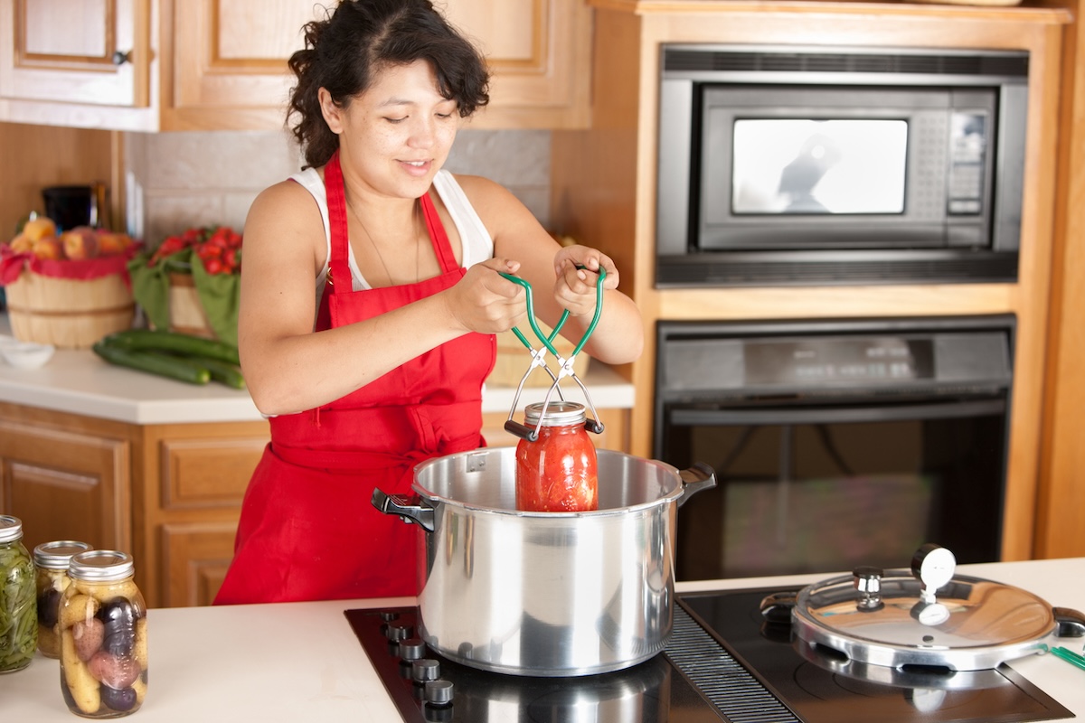 Woman in apron cans tomatoes.