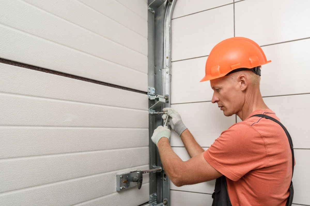 A worker in an orange hard hat uses a tool to fix a garage door. 