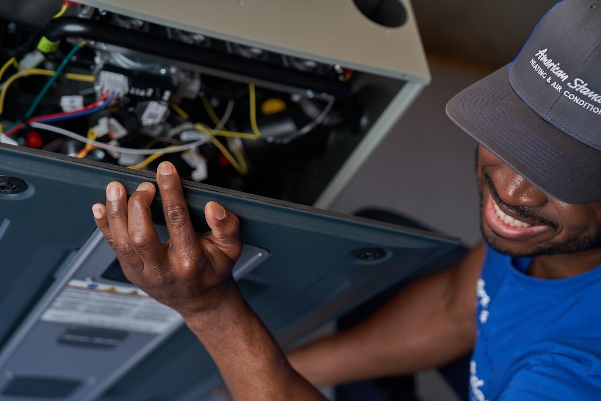 An American Standard HVAC expert opening a heat pump unit and installing one in a residential home.