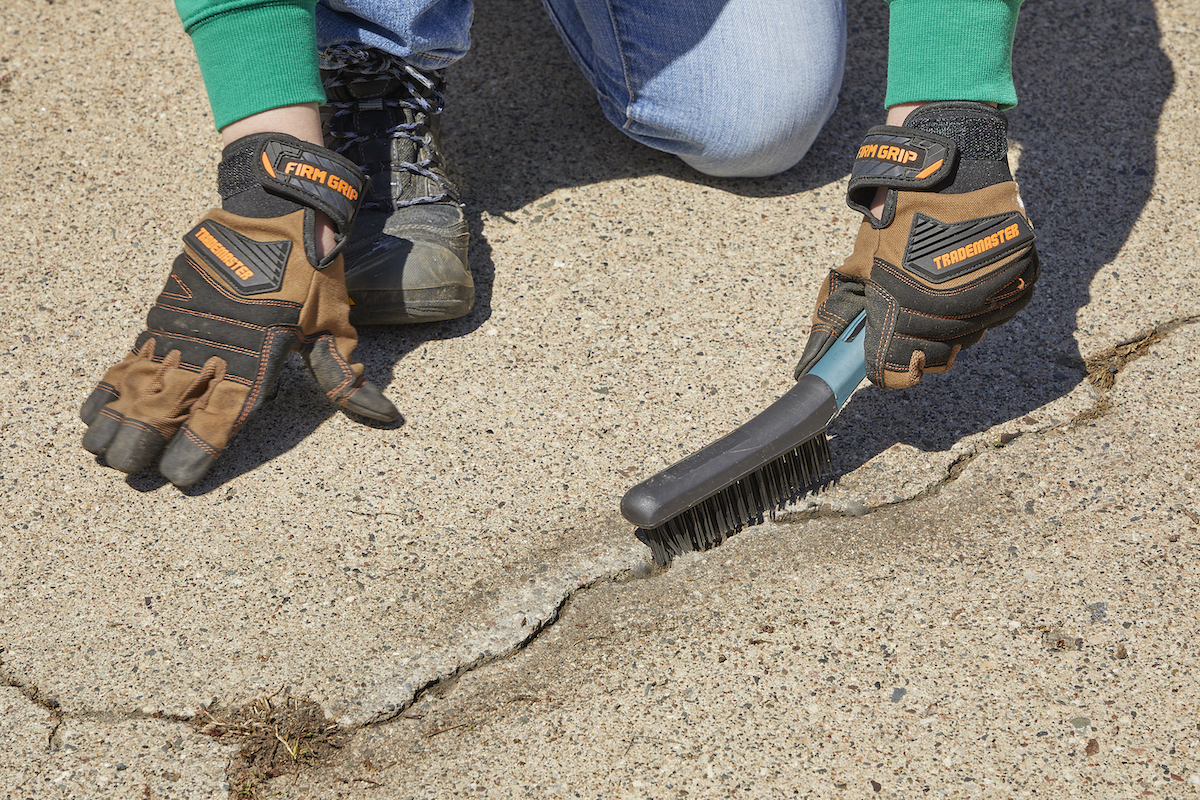 Woman uses wire brush to clear debris out of a crack in concrete.