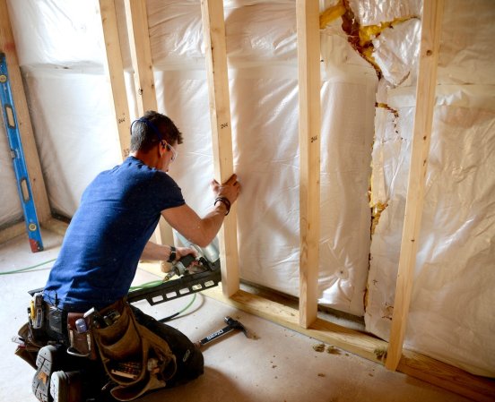 Person in blue shirt framing a wall.