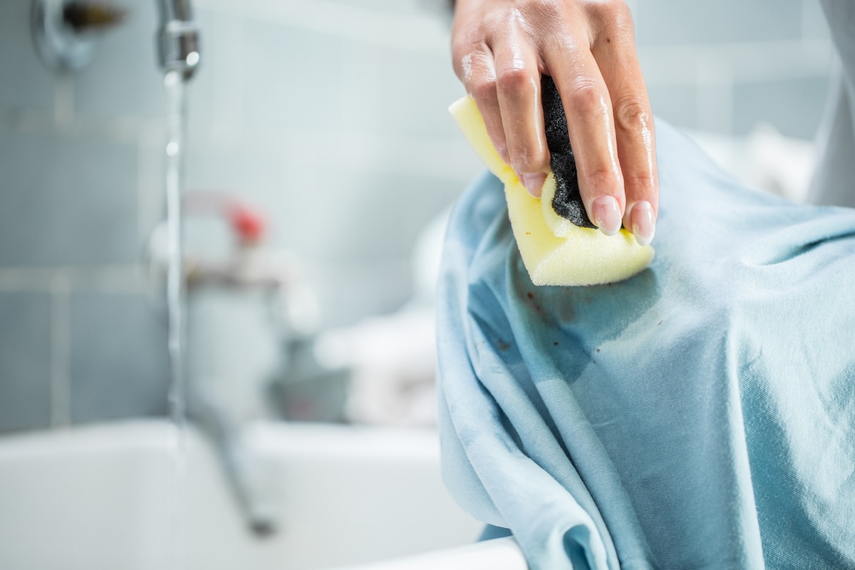 A person pretreating laundry stains before adding garment to washing machine.