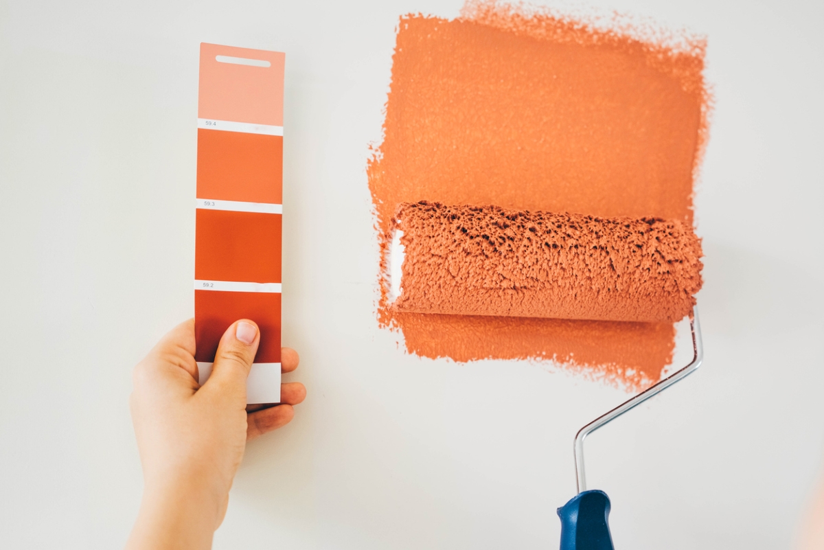 Person holding paint swatch next to paint roller on wall.