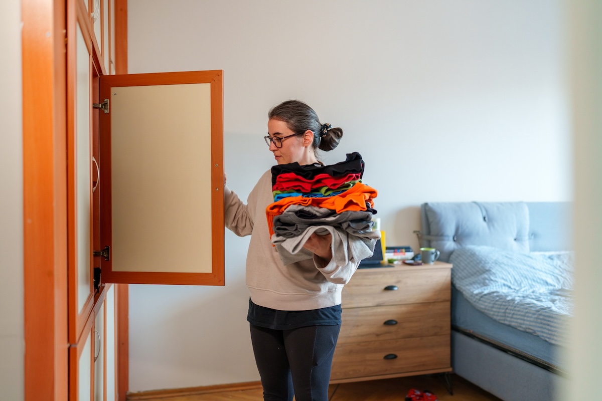 A person putting away folded laundry in a bedroom.