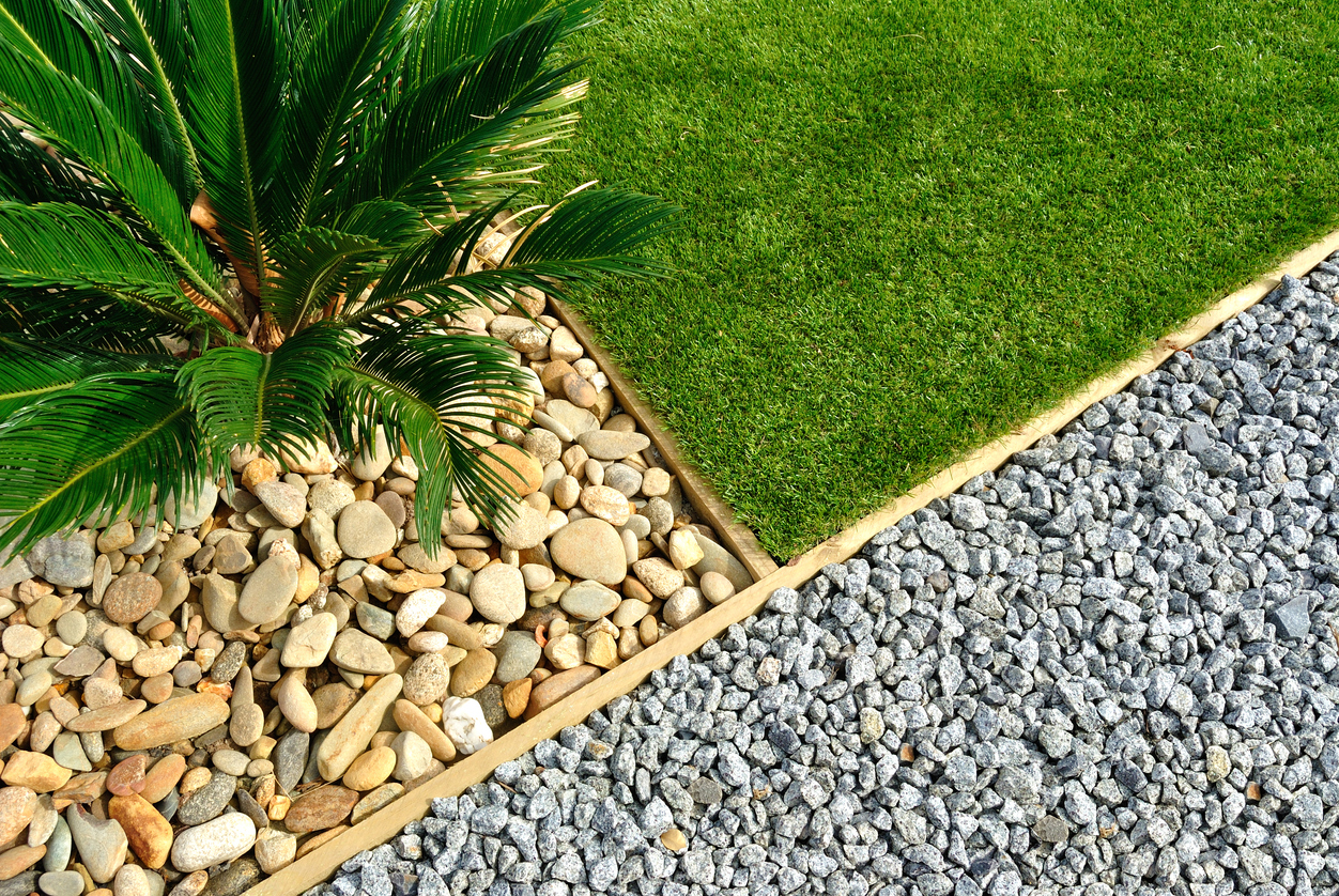 A manicured yard intersected with a rock garden of smooth yellow stones with a large plant and a rock garden of small grey rocks.