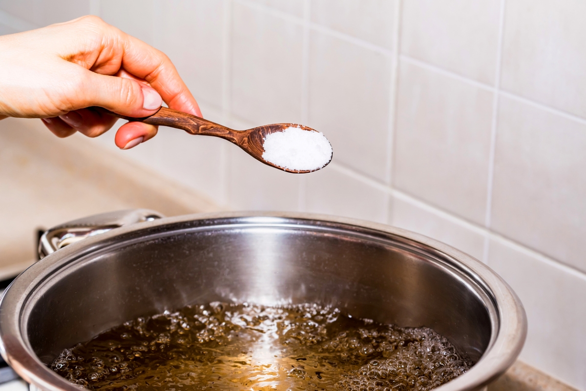 A hand adding baking soda to boiling water.