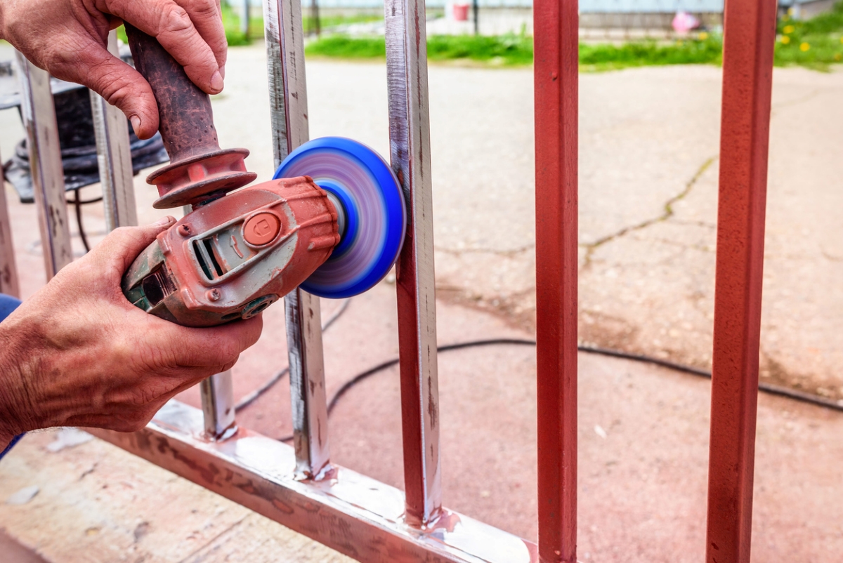 Person using angle grinder to remove red paint on from metal fence.