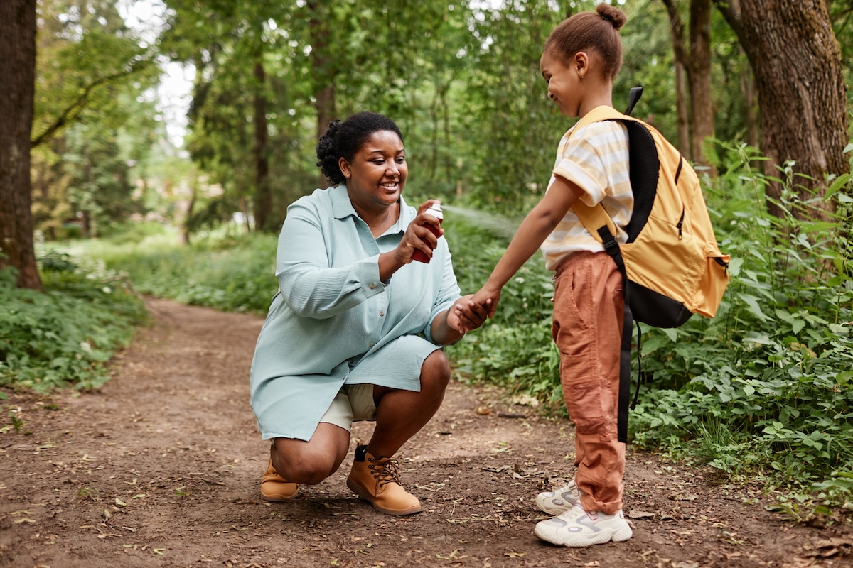 Mother on hiking trail spray mosquito repellant on child.