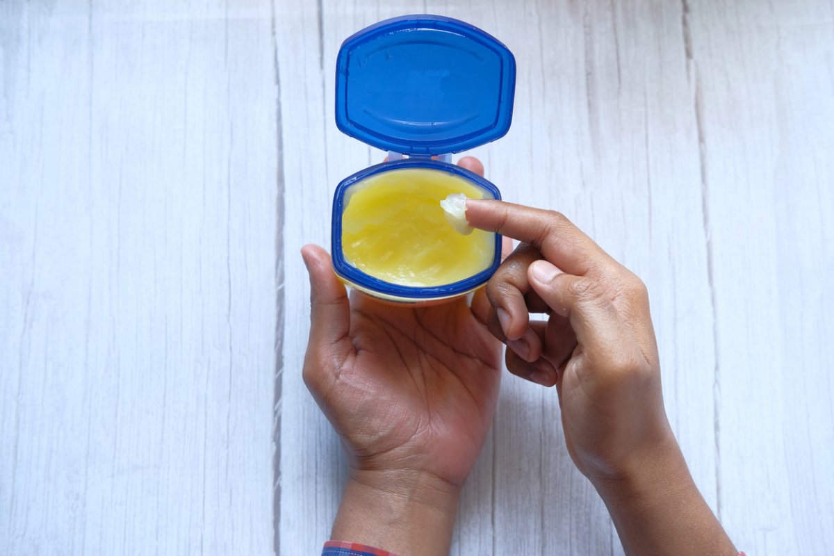 Bird's eye view of a man holding an open jar of petroleum jelly in his hand, with a daub on a finger.