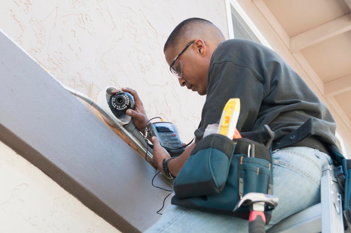 A worker stands on a ladder to install a security camera.