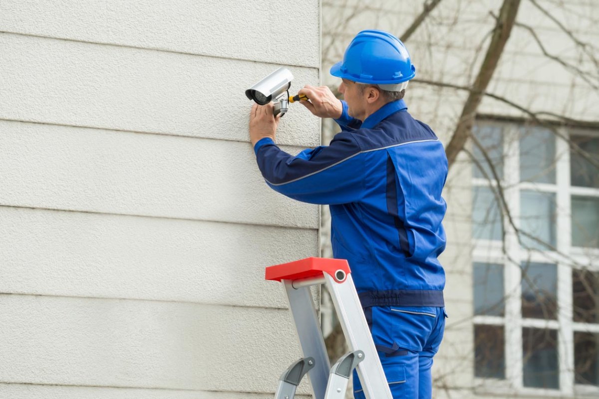 A worker in a blue hard hat installs a security camera. 