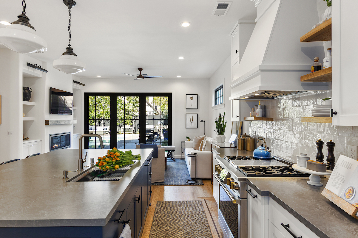 A kitchen features hardwood flooring, a navy kitchen island, and white tiled backsplash.