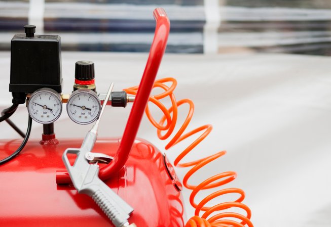 A red horizontal air compressor's air tool and pressure gauges.