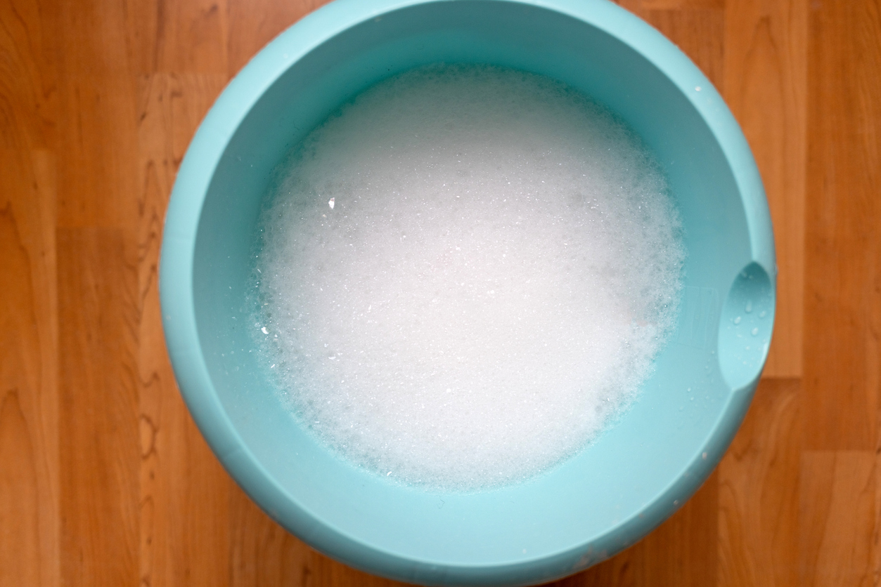 A light-blue bucket is half-filled with a soapy water solution.