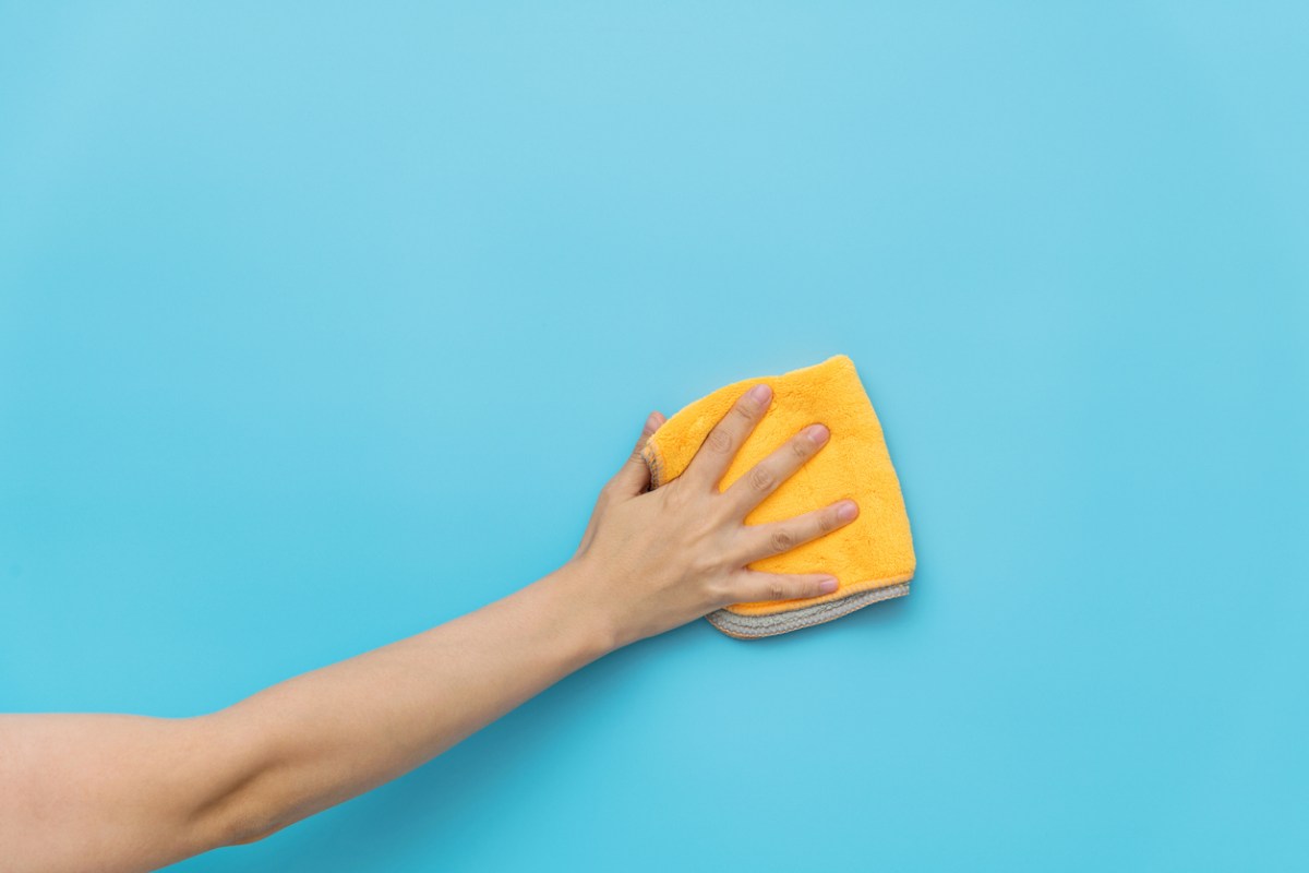 A person wipes a flat blue wall with a dry microfiber cloth.