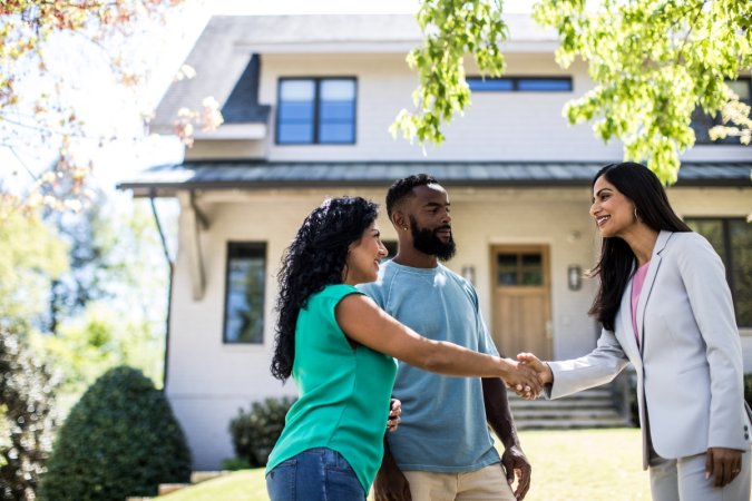 A couple is meeting their realtor outside of a house.