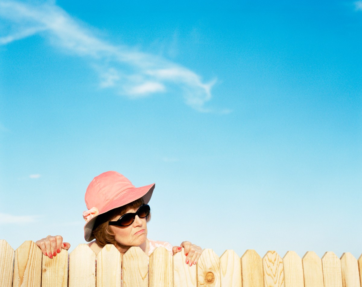 Woman-wearing-a-pink-hat-looks-over-a-picket-fence-with-an-annoyed-facial-expression.