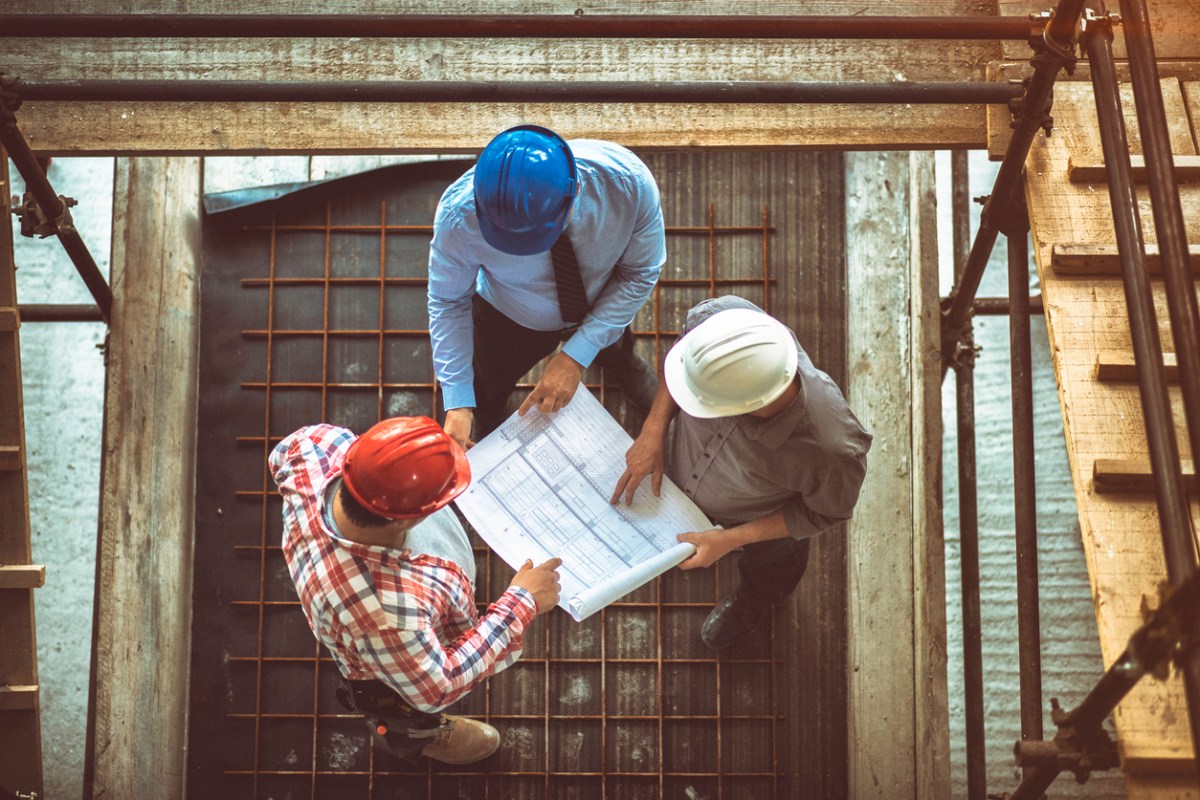 An aerial view of three workers consulting a building plan.