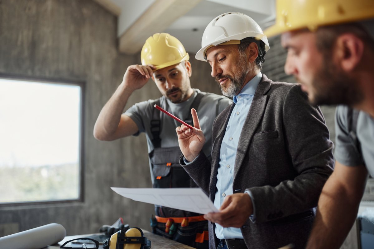 Three workers in hard hats consult a building plan. 