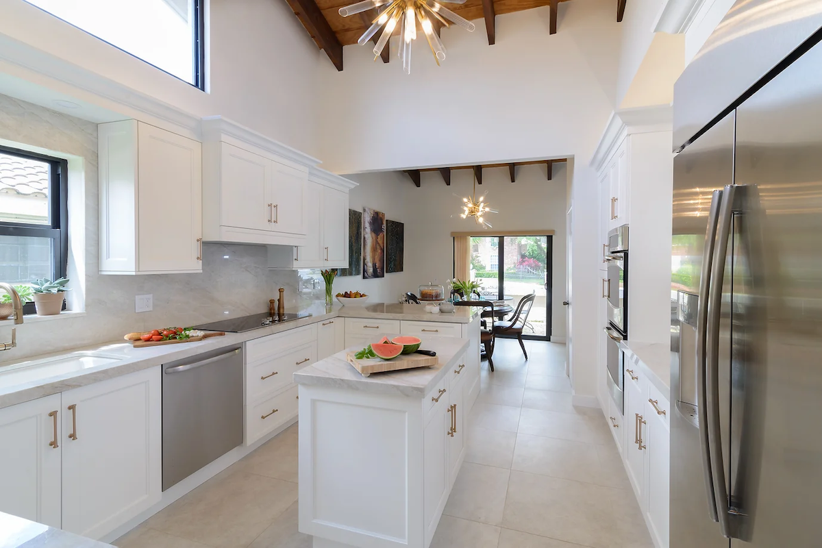 A white kitchen with quartz countertops features stainless steel appliances and cutting boards with prepared fruits and vegetables.