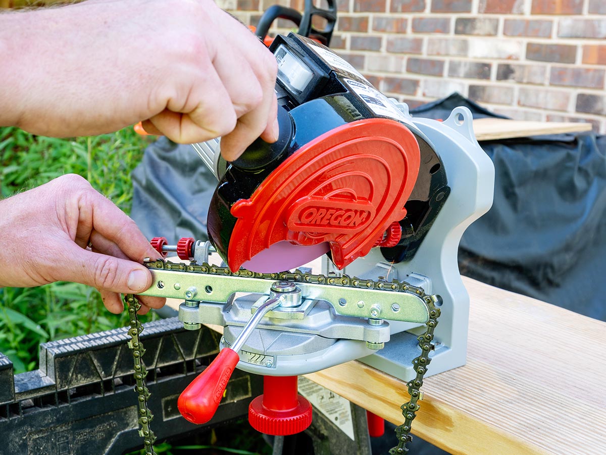 A person using the Oregon 410-120 Bench Grinder Chain Sharpener to sharpen a chainsaw chain during testing.