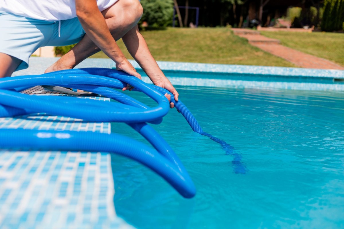 A close up of a person lowering a hose into a pool.