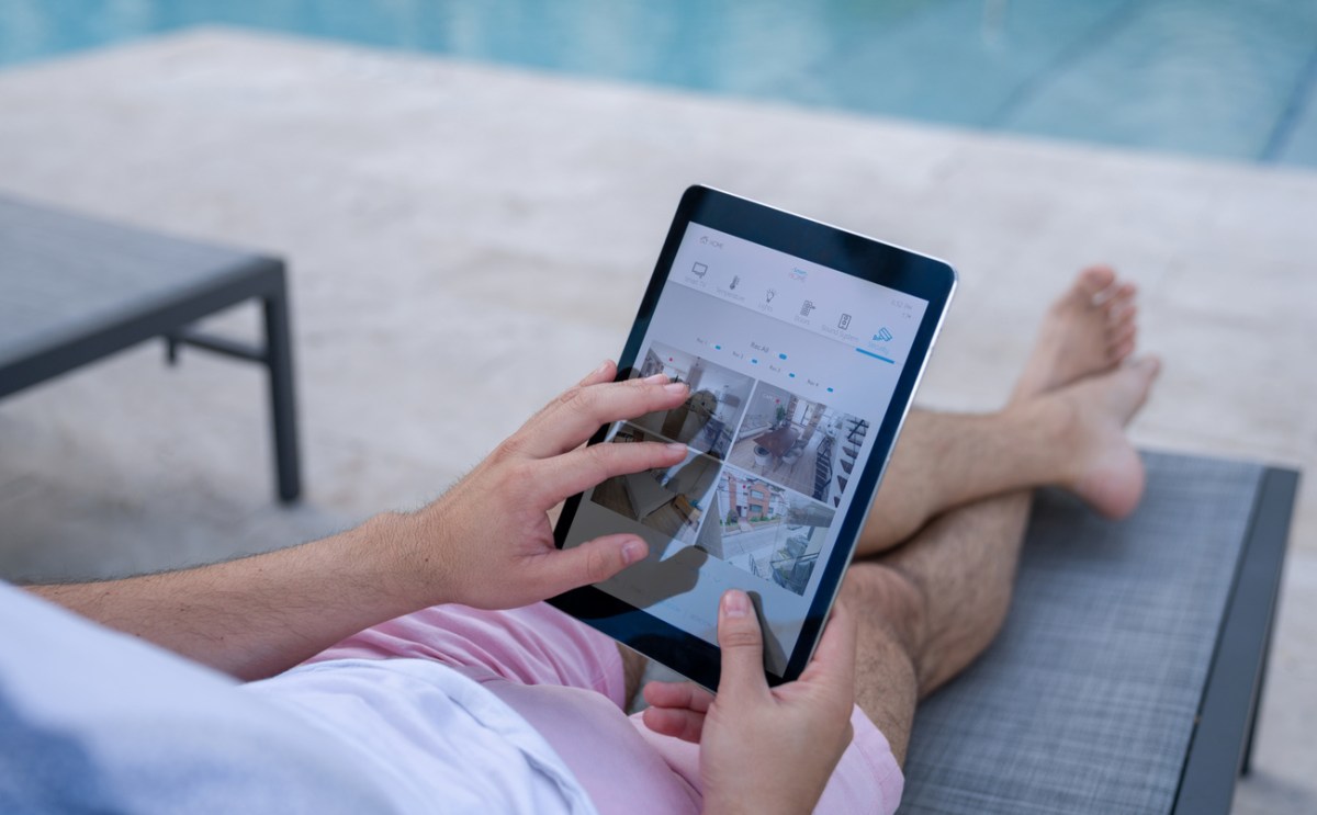 A person lounging by a pool accesses safety camera footage seen on a tablet. 