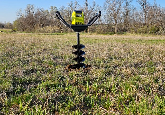 The Ryobi RY40710 Cordless Earth Auger partially embedded in a field during testing.
