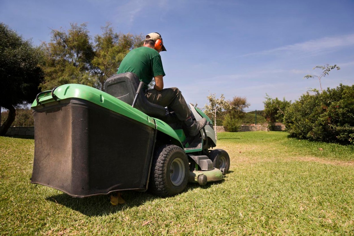 A worker in a green shirt rides a riding lawn mower. 