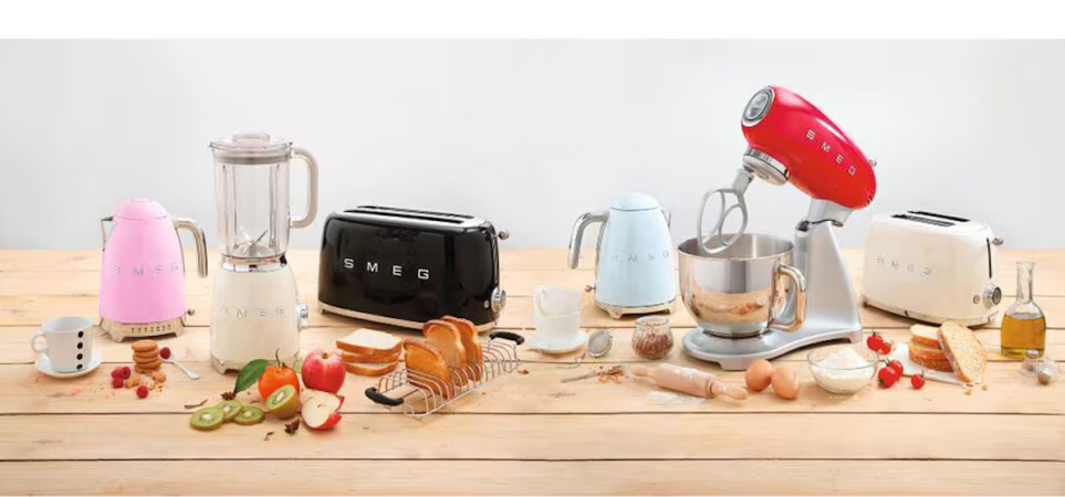 An assortment of colorful countertop appliances by Smeg sit on a wooden counter.