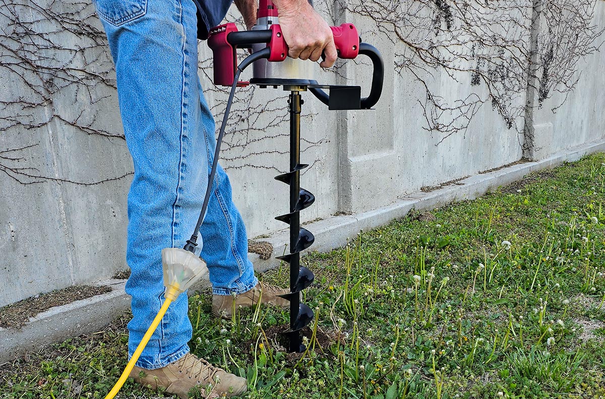 A person using the  Earthquake 2-Person Earth Auger Powerhead to dig a post hole during testing.