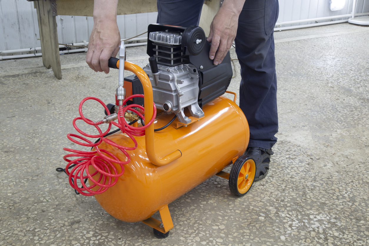 A person prepares an orange horizontal air compressor for use.