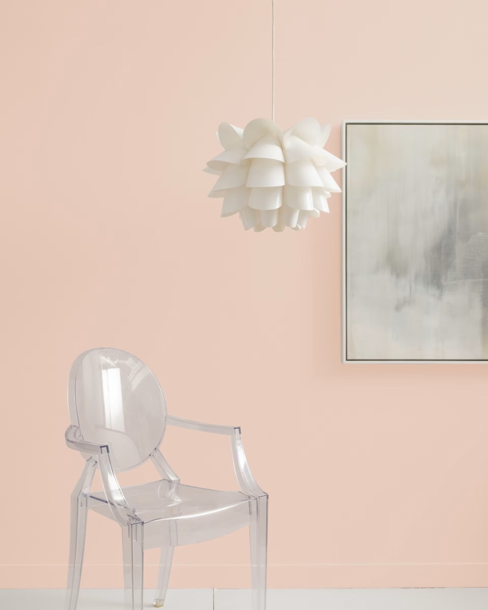 A clear chair in front of a pale pink wall.