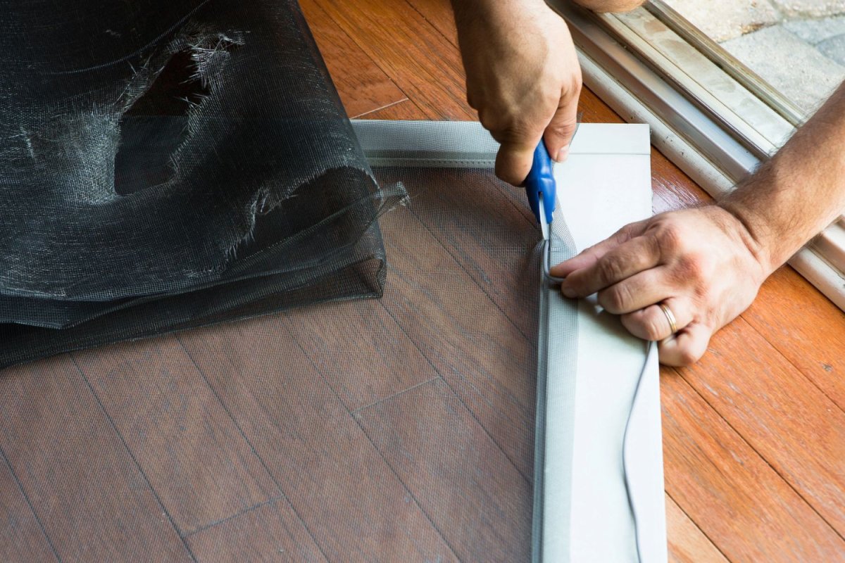 A view of a person cutting a screen of a patio door. 