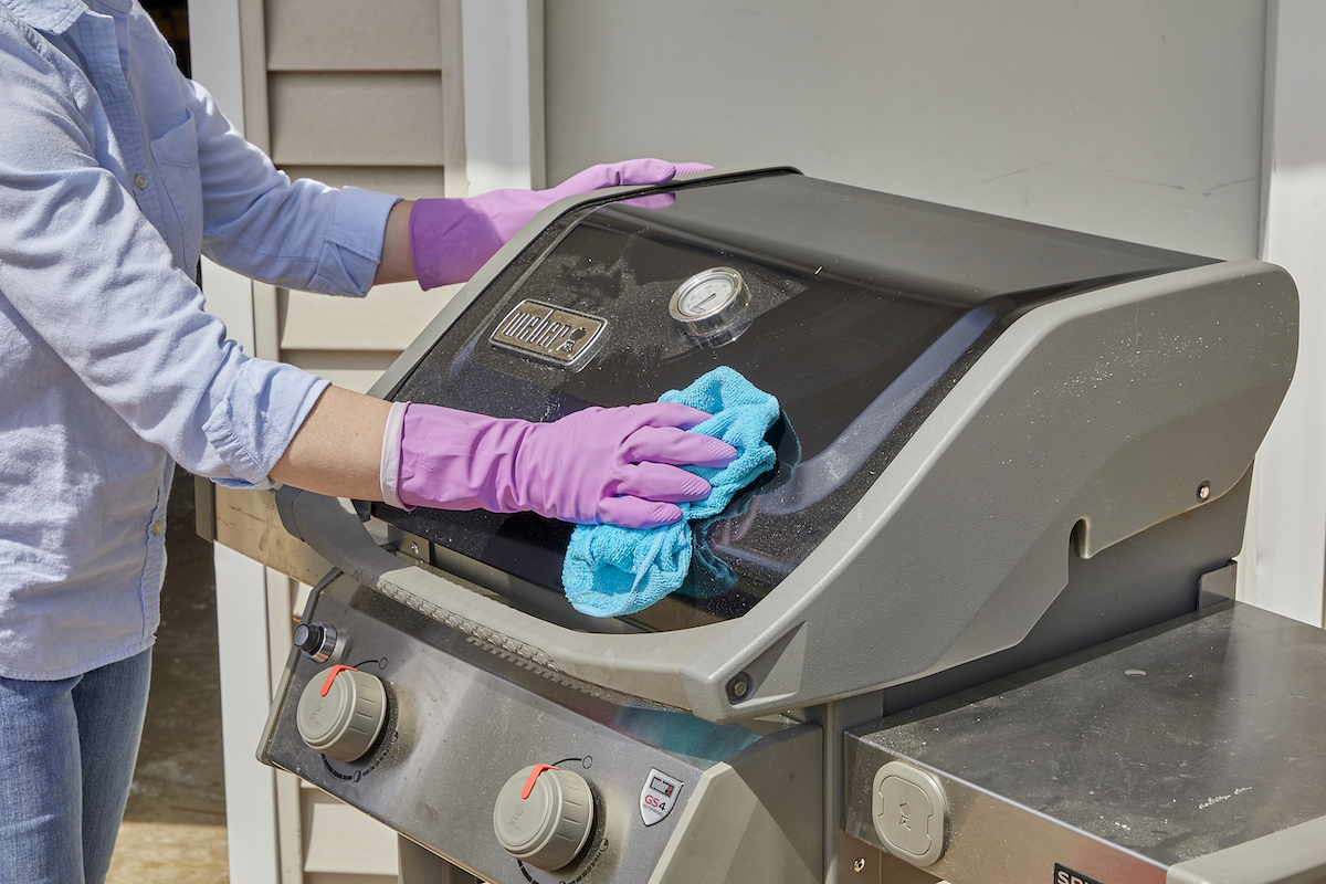 Woman wipes the exterior hood of a gas grill with a microfiber cloth.