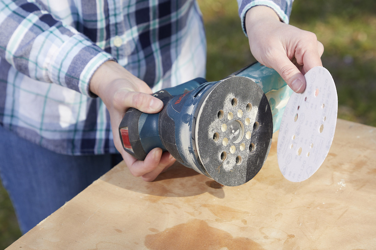 Woman attaches a sandpaper disc to a palm sander.