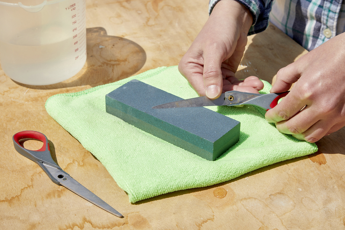 Woman sharpens the second scissor blade on a sharpening stone. 