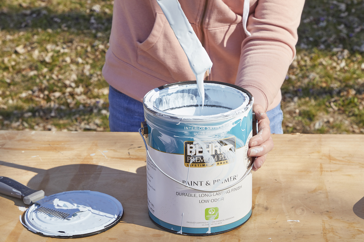 Woman pulls a paint stick out of a gallon of white paint, showing that the paint is too thick.