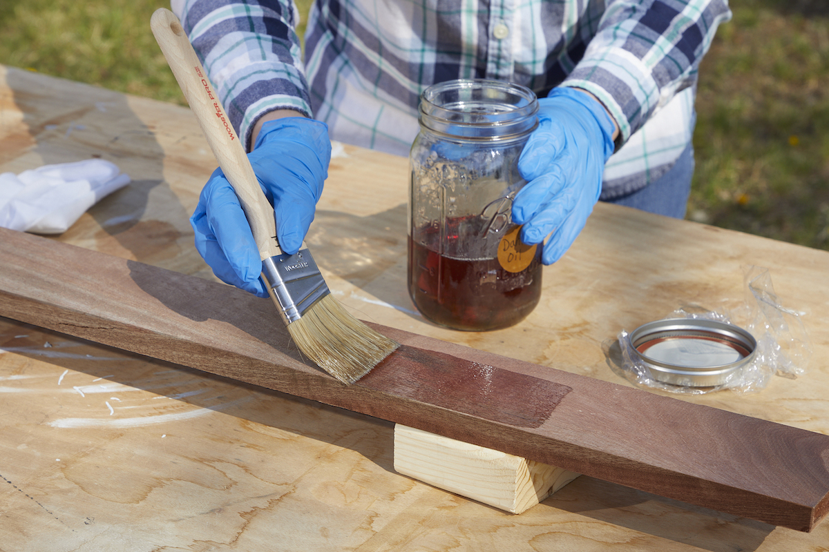 Woman uses natural-bristle paint brush to apply an oil sealant to wood board.